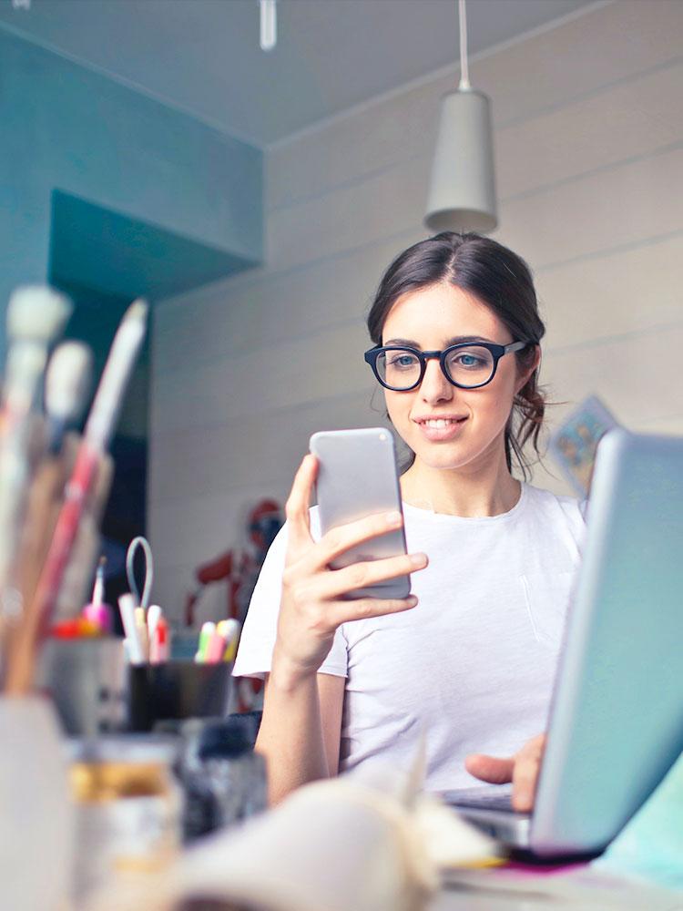 Jeune femme en télétravail, elle regarde son portable et son ordinateur portable est sur la table