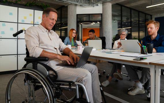 Personne en fauteuil roulant entrain de travailler avec d\'autres collaborateur dans une collectivité